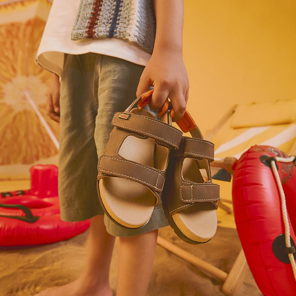 Niño cargando unas sandalias infantiles Coqueta y Audaz, calzado cómodo y fresco ideal para primavera verano, listo para jugar y disfrutar los días de sol.