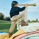 Niño con botas Coqueta y Audaz explorando con catalejo sobre colchonetas de colores. Colección Pisa Fuerte, botas para conquistar el mundo.